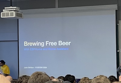 A lecture hall with a presentation slide that reads "Brewing Free Beer with ESPHome and Home Assistant"